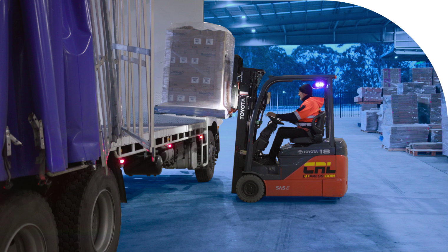 Man operating a forklift to load cargo onto a truck in a logistics operation